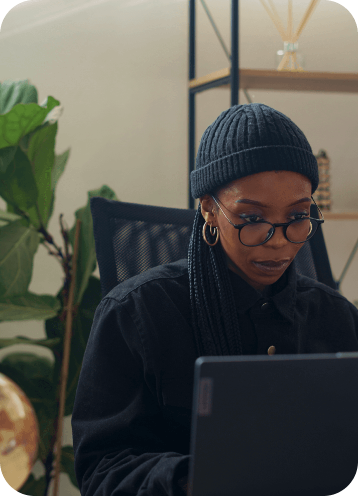 A woman working on a laptop in front of a plant.